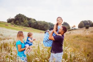 Family plays with children on the field with white flowers